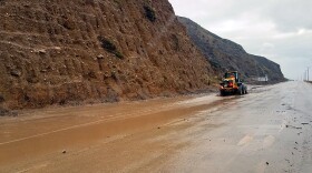 This photo provided by the California Department of Transportation (CalTrans) shows a skiploader clearing a river of mud that has flowed onto Pacific Coast Highway in Malibu, Calif., Monday, Jan. 14, 2019. The first in a series of Pacific storms is moving across Southern California, where downpours could unleash mud and debris flows from large wildfire burn scars.