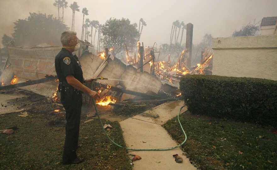 A San Diego Police officer uses a garden hose to try to save a home next to a burning one in the community of Rancho Bernardo, San Diego, Calif., Monday, Oct 22. 2007.