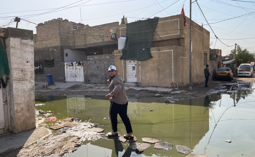 Electoral candidate Taghrid Mohammed Alkhazali crosses a street filled with sewage mixed with wastewater in a Baghdad slum. She is from a new political party that is running on a platform promoting better public services for Iraqis.