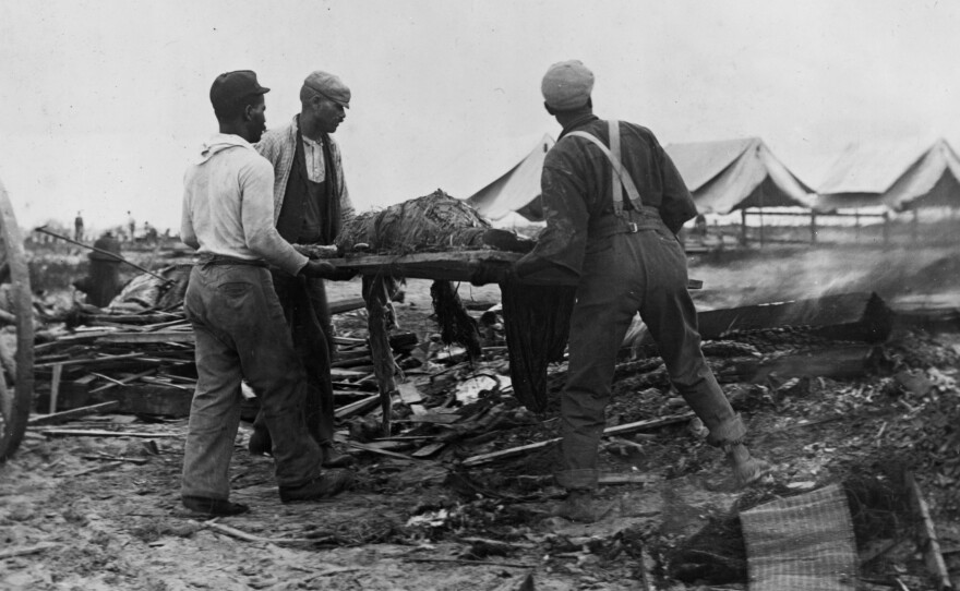 Men carry a body on a stretcher, surrounded by wreckage of the hurricane and flood in Galveston.