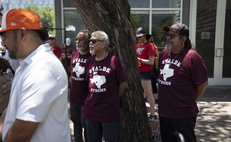 Men with t-shirts reading "Uvalde strong," in honor of the school shooting, attend a protest outside.