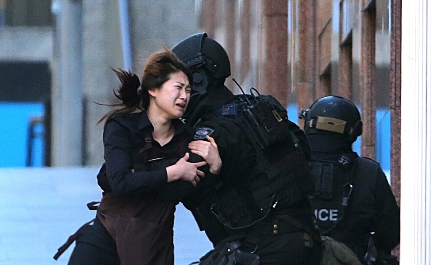 A hostage runs to armed tactical response police officers for safety after she escaped from a cafe under siege at Martin Place in the central business district of Sydney, Australia, on Monday.