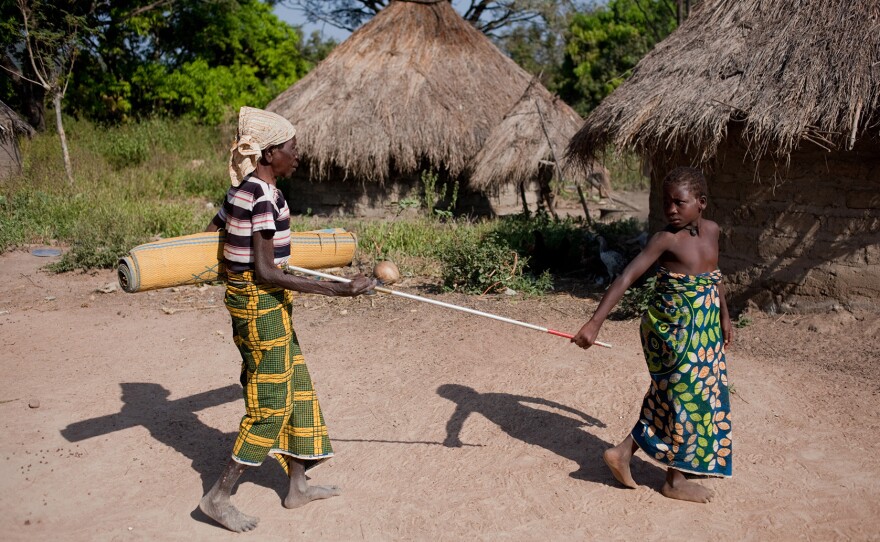 An elderly Nigerian woman who suffers from river blindness is helped by a young girl.