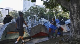 In this Monday, July 1, 2019 file photo, homeless people move their belongings from a street along side of Los Angeles City Hall as crews prepared to clean the area. 