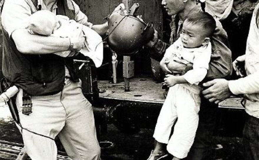 A sailor helps a man and a baby in Operation Frequent Wind on the USS Midway, April 29, 1975.