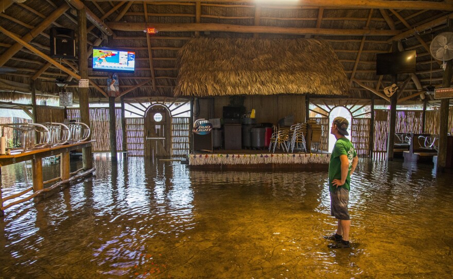 Brian Mugrage watches the weather on TV as he stands in the storm surge inside the Riverside Cafe in St. Marks, Fla., on Thursday.