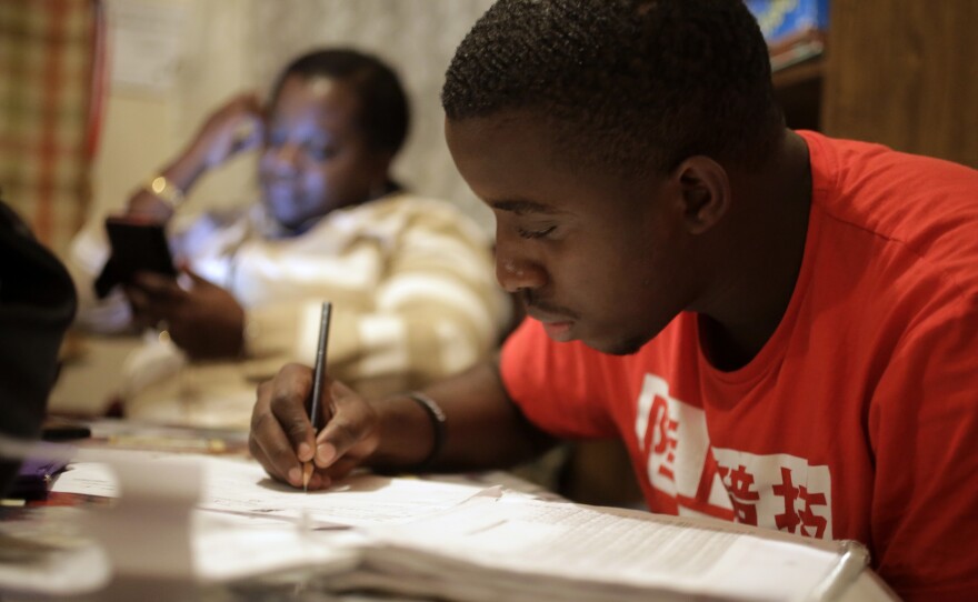 In this Wednesday, Nov. 15, 2017 photo, Amocachy Jeune, right, does homework as his mother Marianne Jeune, left, a Haitian immigrant staying in the U.S. through the Temporary Protected Status program, sits nearby at their Boston home.