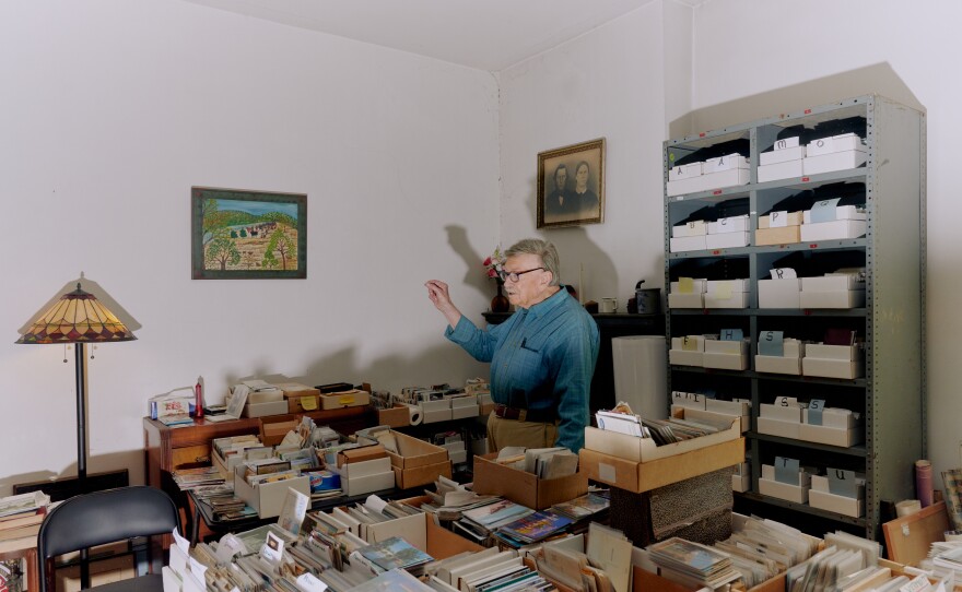 Brown poses for a portrait inside his home surrounded by some of his many postcards.
