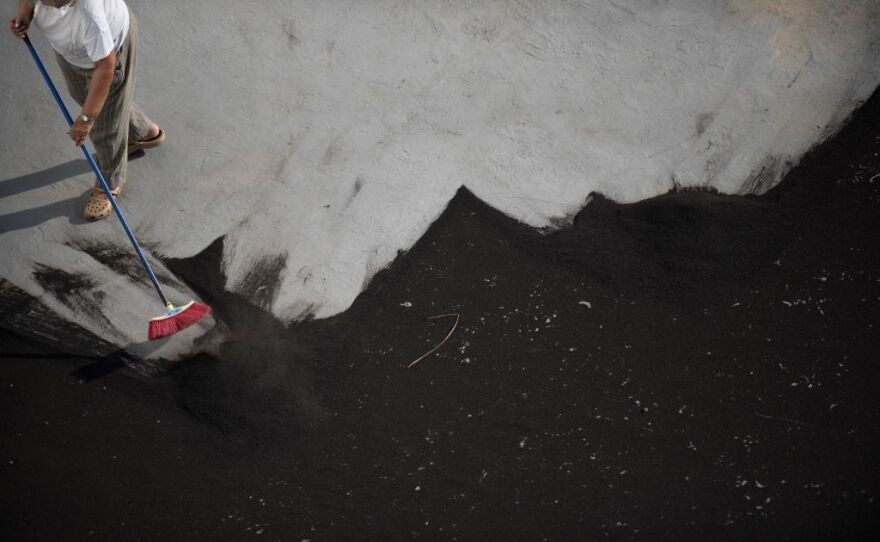 A man sweeps ash spewed by the La Palma volcano off the roof. Authorities say a 72 year old man died while cleaning ash from his home. Residents say the ash has made it difficult to breathe.