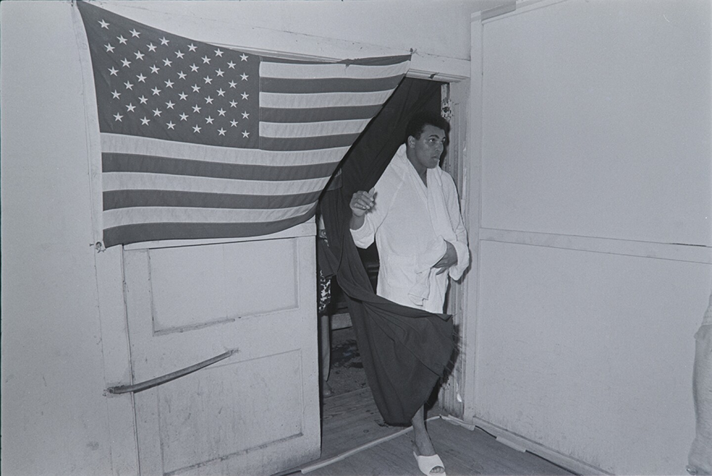 Muhammad Ali coming through doorway draped in a United States flag. Fifth Street Gym. Miami, Fla. Feb. 25, 1971.