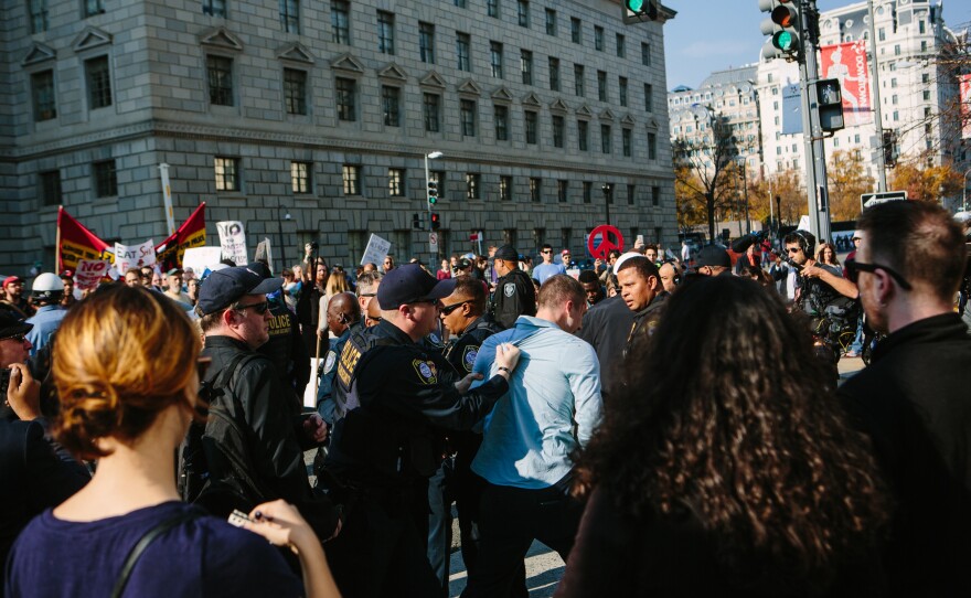 Protesters along 14th Street outside of the Reagan Building shout as police escort a man from the crowd after a brief confrontation.