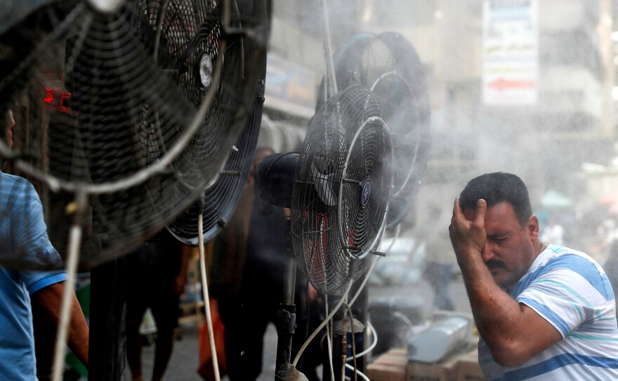 Fans spray air mixed with water vapor to cool down pedestrians on a Baghdad street on June 30, 2021, during a heat wave.