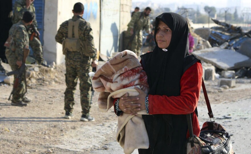 A Syrian woman carries her belongings past Kurdish fighters as she flees on Sunday. The Syrian Observatory for Human Rights says shelling has killed 26 people who were trying to flee eastern Aleppo.