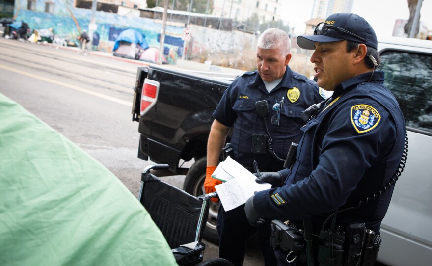 San Diego police give a citation to a woman camping on the sidewalk of Commercial Street in San Diego, June 9, 2022.