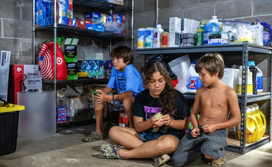 Caleb, 11, Bella, 12, and Nash Cabanilla Okano, 8, sit in a supply room at the house where they're taking shelter after their homes were destroyed.