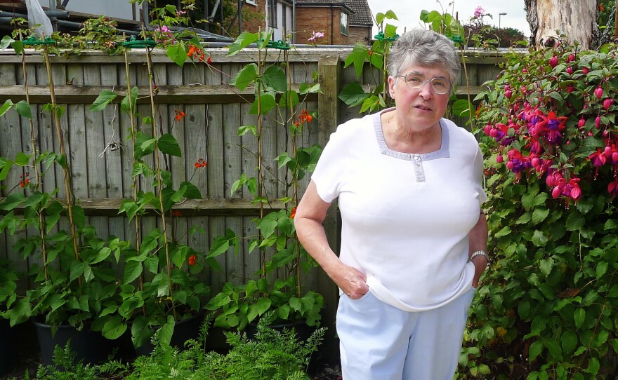 Fran Beesley stands next to the flowers in her yard, where she recently found a Japanese family taking photos. The small English village where she lives, Kidlington, was inundated by Asian tourists earlier this summer, and no one knows why.