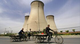 Workers ride past cooling towers at a coal-fired power plant on the outskirts of Beijing. Such power plants are at the center of a debate about the future of energy production in China and the U.S.