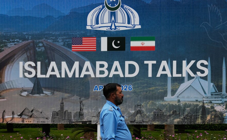 A police officer walks past a billboard regarding the United States and Iran negotiations, outside a media facilitation center in Islamabad, Pakistan, Saturday, April 11, 2026.