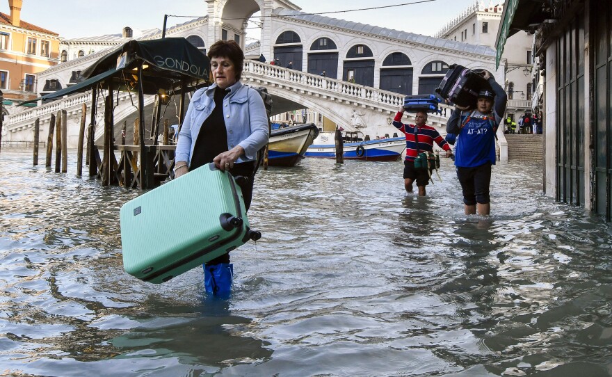 In this Dec. 23, 2019 file photo, people carry their luggage as they wade through water during a high tide of 1.44 meters (4.72 feet), near the Rialto Bridge, in Venice, Italy.