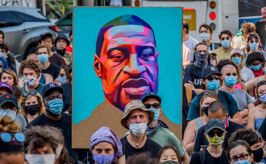 Protesters hold a portrait of George Floyd at a demonstration against police brutality in New York City. Policing "wasn't always this big. It wasn't always this bureaucratic," journalist Jamiles Lartey says.