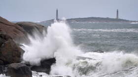 Surf breaks along the rocky coastline, with the twin lighthouses of Thatcher Island visible in the distance, during the early stages of a nor'easter Friday, Sept. 25, 2026, in Gloucester, Mass.