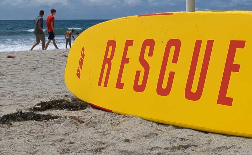 Two men walking in front of a lifeguard's rescue surfboard at the beach in Del Mar, Calif., June 12, 2023.