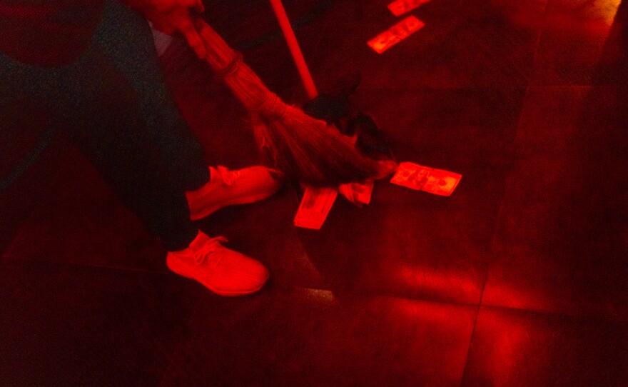 A woman sweeps up fake hundred dollar bills and broken glass after a cocktail fell on the dance floor.