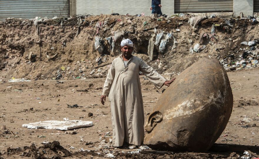 An Egyptian worker stands next to the head of a statue at the site of a new discovery by a team of German-Egyptian archaeologists in Cairo's Matariya District.