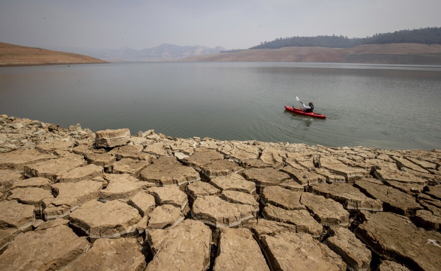 In this Aug. 22, 2021, file photo a kayaker fishes in Lake Oroville as water levels remain low due to continuing drought conditions in Oroville, Calif.