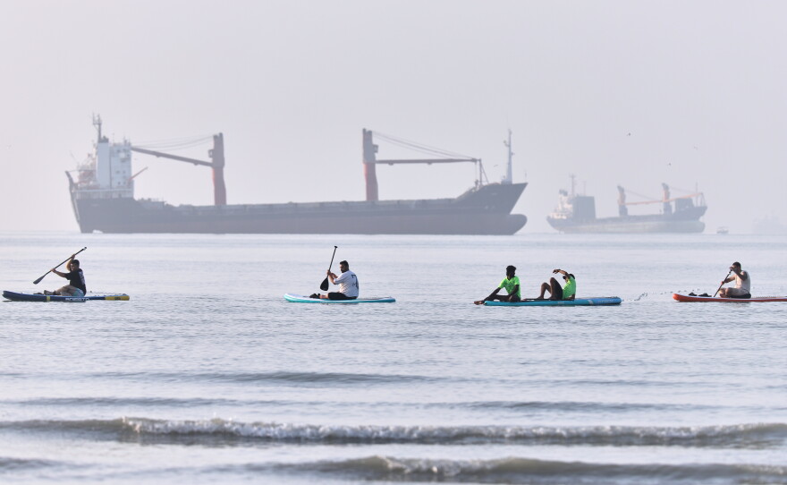People paddle along the shoreline as cargo ships are anchored in the Strait of Hormuz off Bandar Abbas, Iran, on Monday.