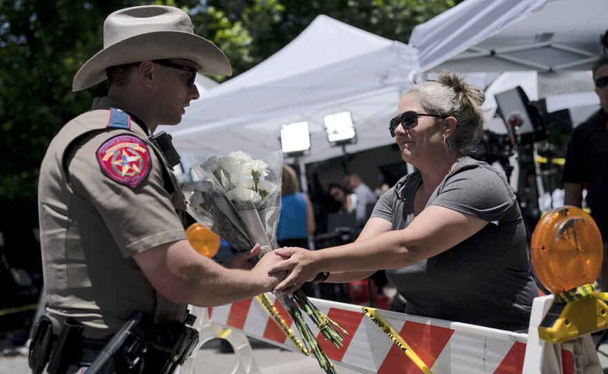 Sheena Rodriguez on Wednesday hands a state trooper a bouquet of flowers, honoring the victims killed in Tuesday's school shooting in Uvalde, Texas.