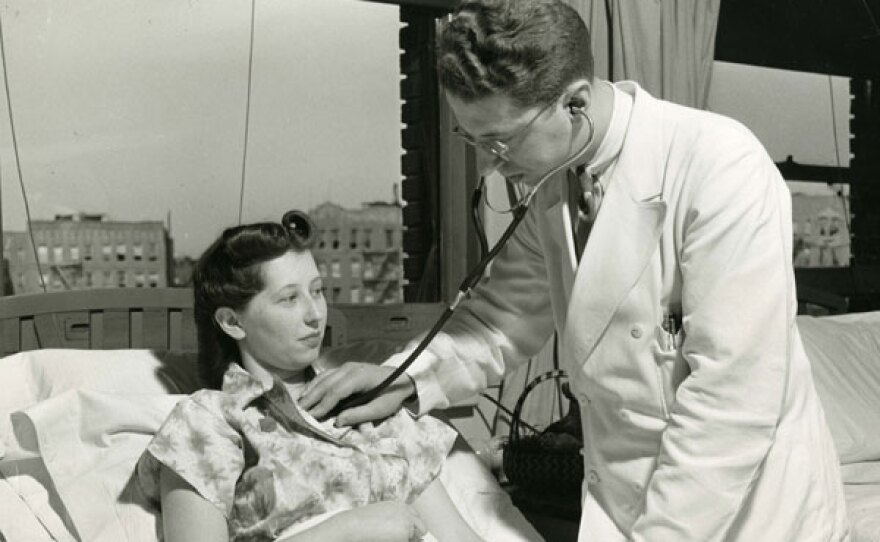 A doctor listens to the heart of a female patient on bed rest.