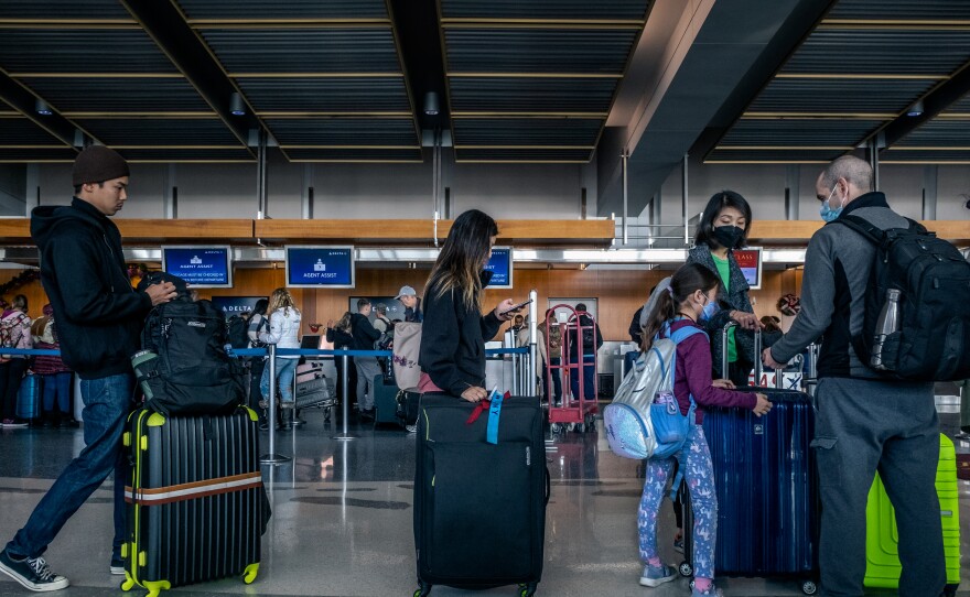 Travelers, some wearing masks, wait in long lines to check luggage before going through airport security on their way out of San Diego, Calif. Dec. 23, 2022.