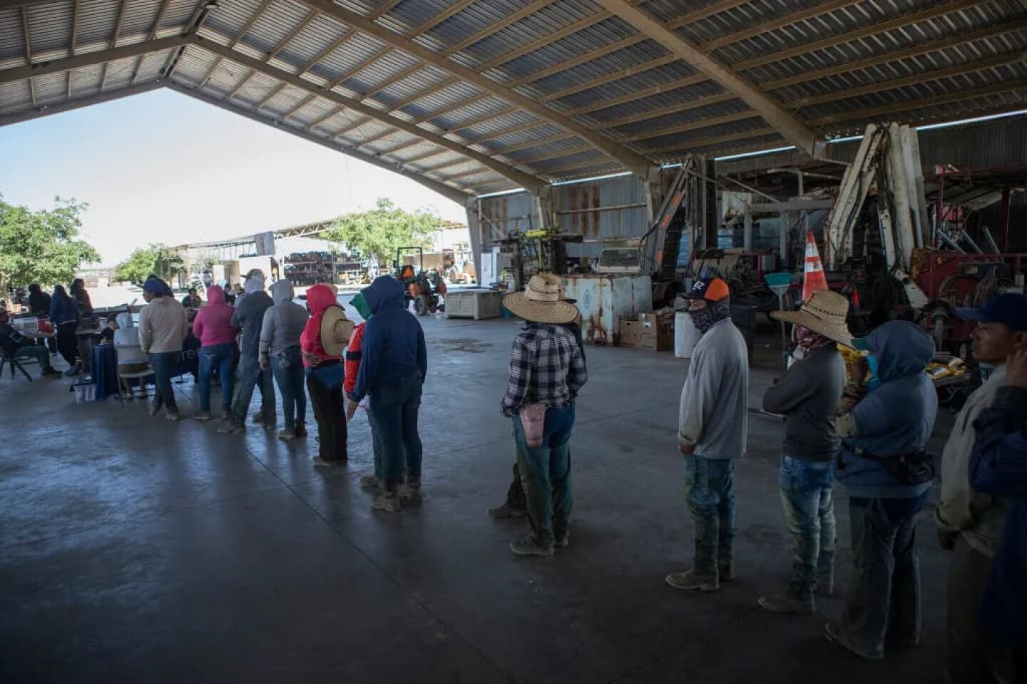 Farmworkers line up in an equipment barn to get a check-up by the staff of UCSF-Fresno, part of the Rural Mobile Health program, at a farm outside of Helm on June 16, 2025.