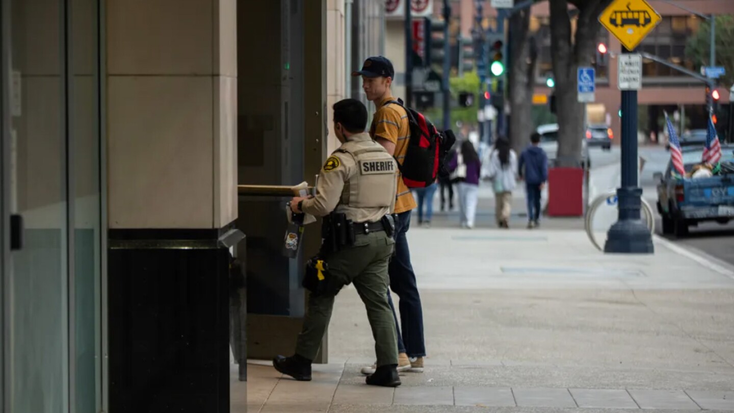 A San Diego sheriff’s employee holds the door for a deputy after scanning his badge to enter the San Diego Central Jail in downtown San Diego on Oct. 24, 2023. 