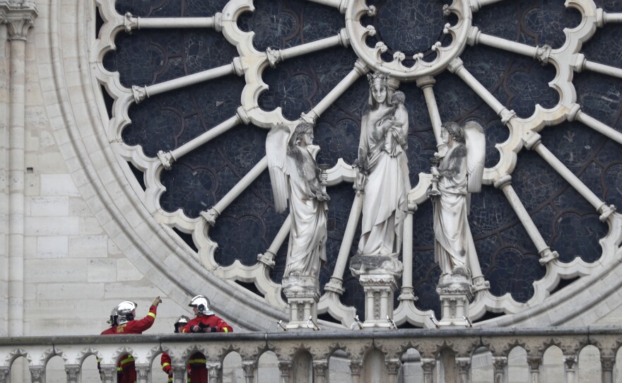 Firefighters talk near the cathedral's rose window on Tuesday. Experts are assessing the blackened shell of Paris' historic cathedral to establish next steps to save what remains.