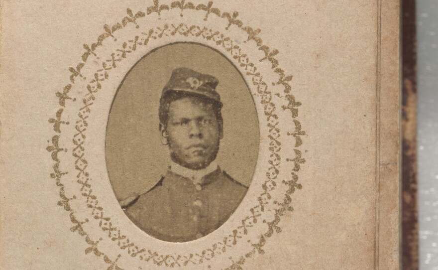 A yellowish brown photograph of Sgt. Isaiah White. He is wearing a buttoned-up jacket with epaulets on the shoulders and a kepi. A bugle insignia is on the front of his kepi. His shoulders are straight and he is directly facing the camera. His kepi is on the left side of his head. His name is inscribed below the photograph on the same page.