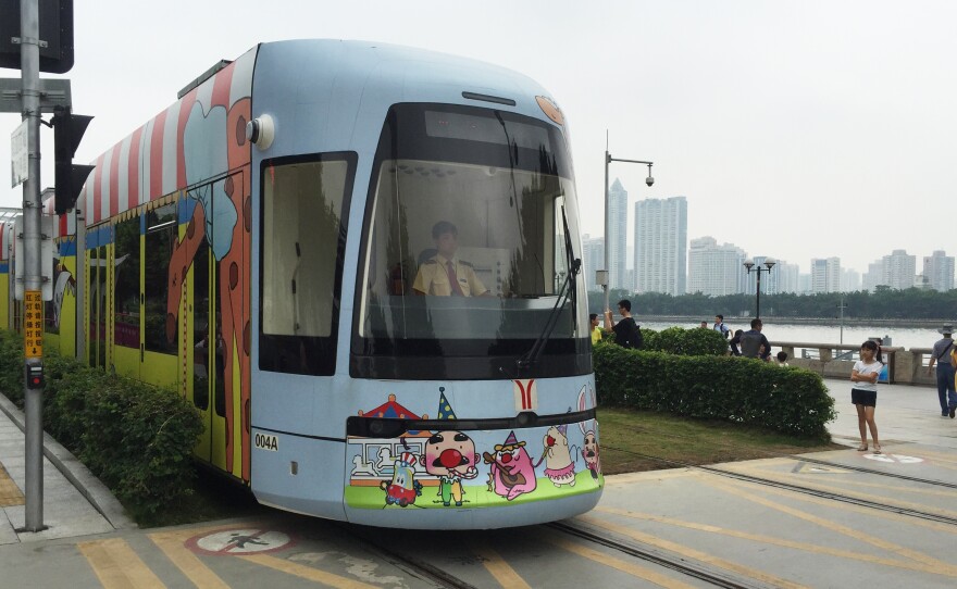 A circus-themed streetcar approaches a pedestrian crosswalk in Guangzhou, China.