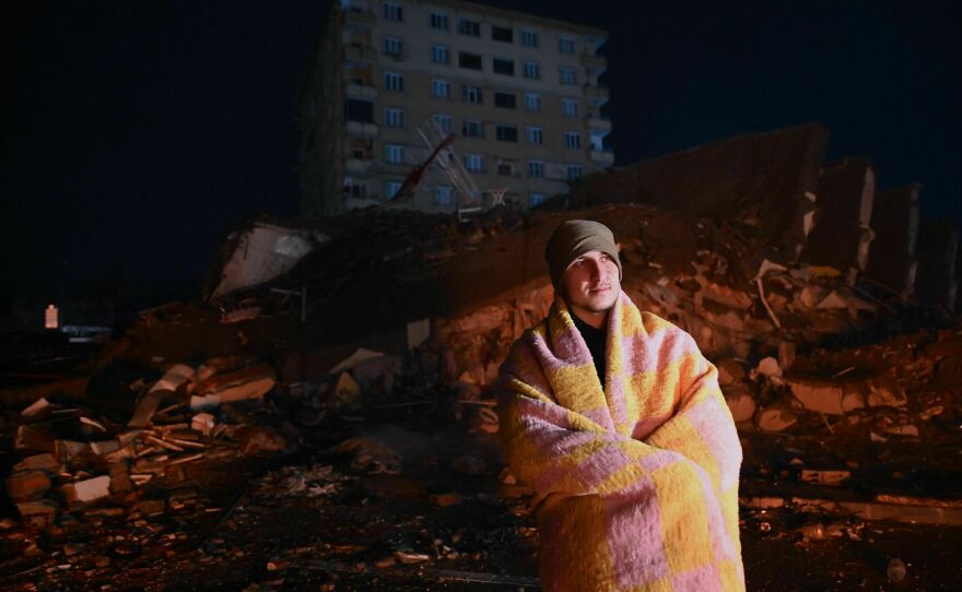 A man looks at rescue personnel searching for victims and survivors through the rubble of buildings in Kahramanmaras, Turkey after a 7.8-magnitude earthquake struck the country's southeast.