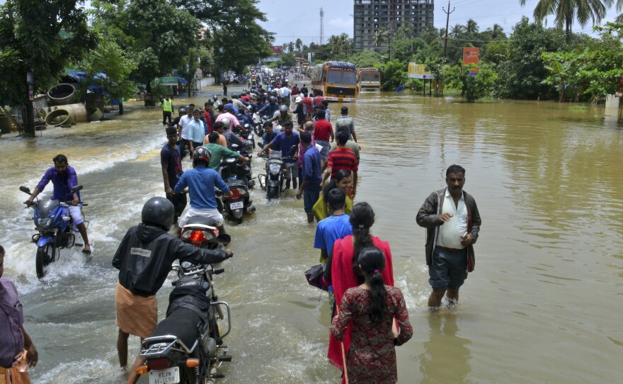 People move past a flooded road in the southern Indian state of Kerala, where monsoon rains have destroyed roads and left hundreds of thousands of people homeless.
