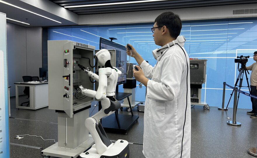 A worker in southern China's Guangzhou city trains a humanoid to push buttons. Eventually robots are expected to take over human tasks.