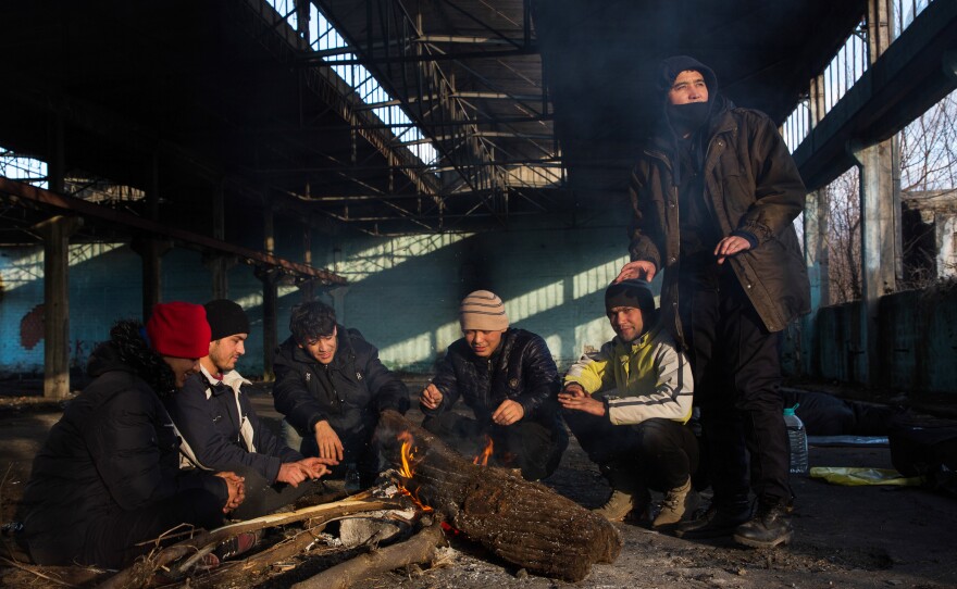 Afghan Morteza Mohammadi (center-left) and his companions sit around a fire in the former Krajina Metal factory in Bihac, Bosnia-Herzegovina, near the Croatian border, discussing possible border crossing strategies related to the weather and time.