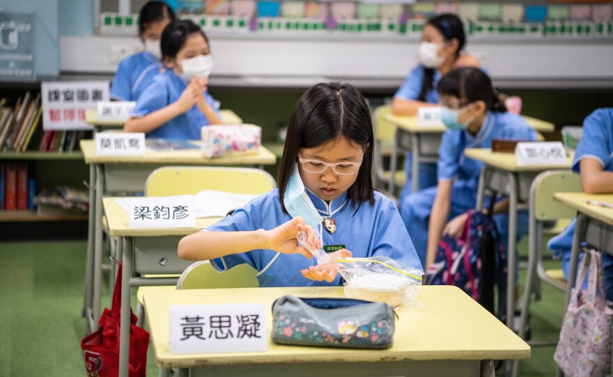 A student takes off her mask and sanitizes her hands before eating her snack.