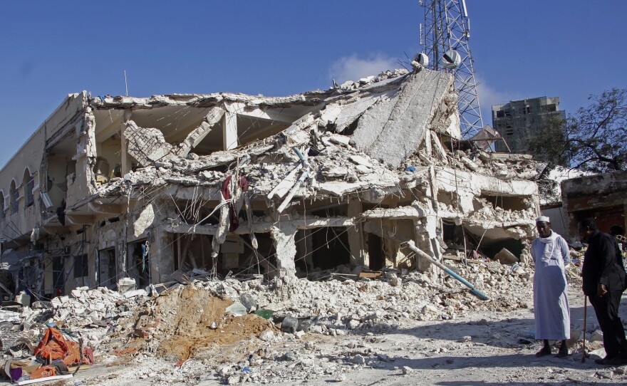 People observe a destroyed building at the scene of Saturday's double car bomb attack at a busy junction in Mogadishu, Somalia.