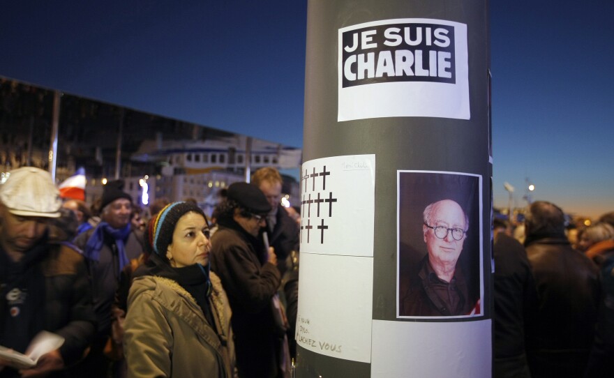 People are shown looking at drawn crosses and the portrait of the French caricaturist Georges Wolinski who was killed during a shooting at a French satirical newspaper in Paris on Jan. 7, 2015.
