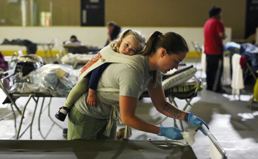 Marlee Hildebrandt and her 2-year-old daughter, Oakley, clean cots at a makeshift evacuee center in Lac la Biche, Alberta, on Thursday, after fleeing forest fires.