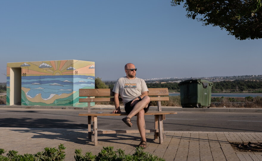 Shahar Goldenberg, Kibbutz Zikim's management member, sits down for a portrait with a bomb shelter behind him.