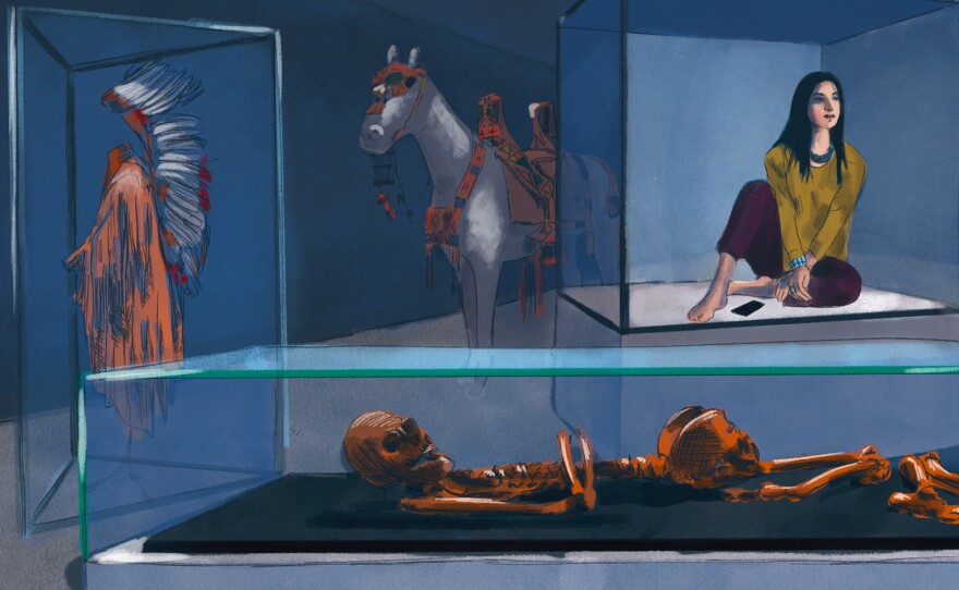 A young Native American woman sits in a museum display case alongside artifacts and human remains.