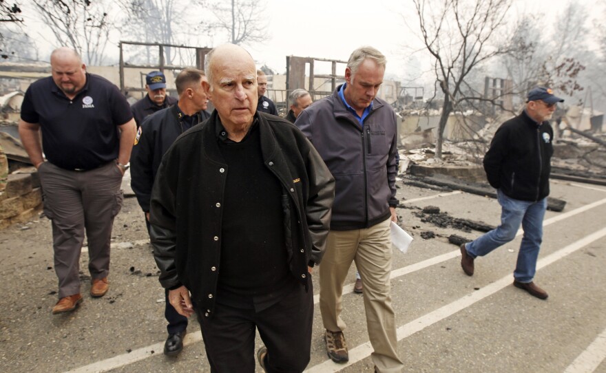 File phot of former Gov. Jerry Brown, center, and former Interior Secretary Ryan Zinke, second from right, tour the Camp-fire ravaged Paradise Elementary School in Paradise, Calif., on Nov. 14, 2018.