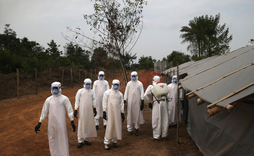 A burial team in Liberia awaits decontamination after performing "safe burials" for people who died of Ebola during the 2014-15 outbreak. Strains of the virus are harbored by bats and primates. A new study looks at how human activity affects the transmission of infectious diseases like Ebola.